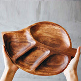 Hands holding acacia wood leaf shaped serving tray with four compartments