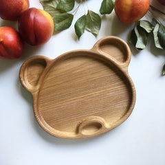 Empty bear shaped wooden kids platter with peaches and leaves on table