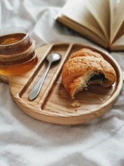 Wooden breakfast tray with bitten croissant, spoon and glass of tea