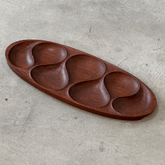 Oval teak wood snack serving tray with five teardrop compartments on concrete surface