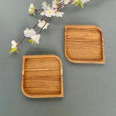 Two square wooden serving platter coaster trays beside white blossoms on grey surface