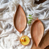 Two leaf shaped wooden platter trays on white cloth with small dish
