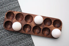 Wooden kitchen egg holder tray holding three white eggs beside grey cloth