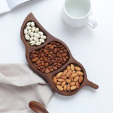Leaf shaped wooden dry fruit snack tray with three sections of nuts beside cup