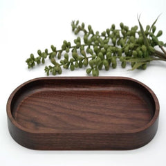 Dark walnut oval wooden serving tray with green plant behind, front view