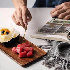 Wooden serving tray holding pink sweets and pastry beside open magazine