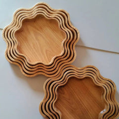 Stack of wavy edge wooden serving platters beside single tray