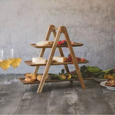 Three-tier wooden food serving tray rack with A-frame stand on dark table