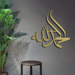 Gold Alhamdulillah Islamic calligraphy wall hanging on dark grey wall beside plant