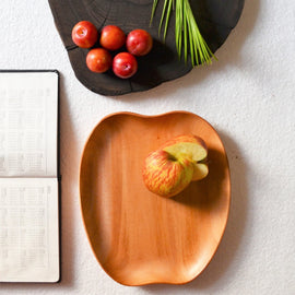 Apple shape wooden platter tray holding fruit beside notebook and tomatoes