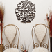 Black round Ayat e Kareema calligraphy wall art above two cream chairs