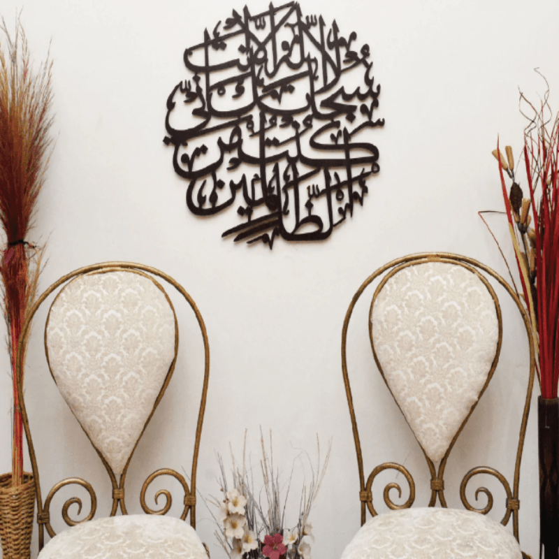 Black round Ayat e Kareema calligraphy wall art above two cream chairs