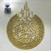 Gold round Ayat ul Kursi calligraphy wall art mounted below wall lamp