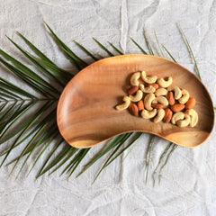 Cashew nut shape wooden platter filled with cashews on palm leaf