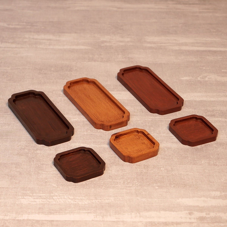Six wooden tea trays in assorted sizes and shades laid out diagonally