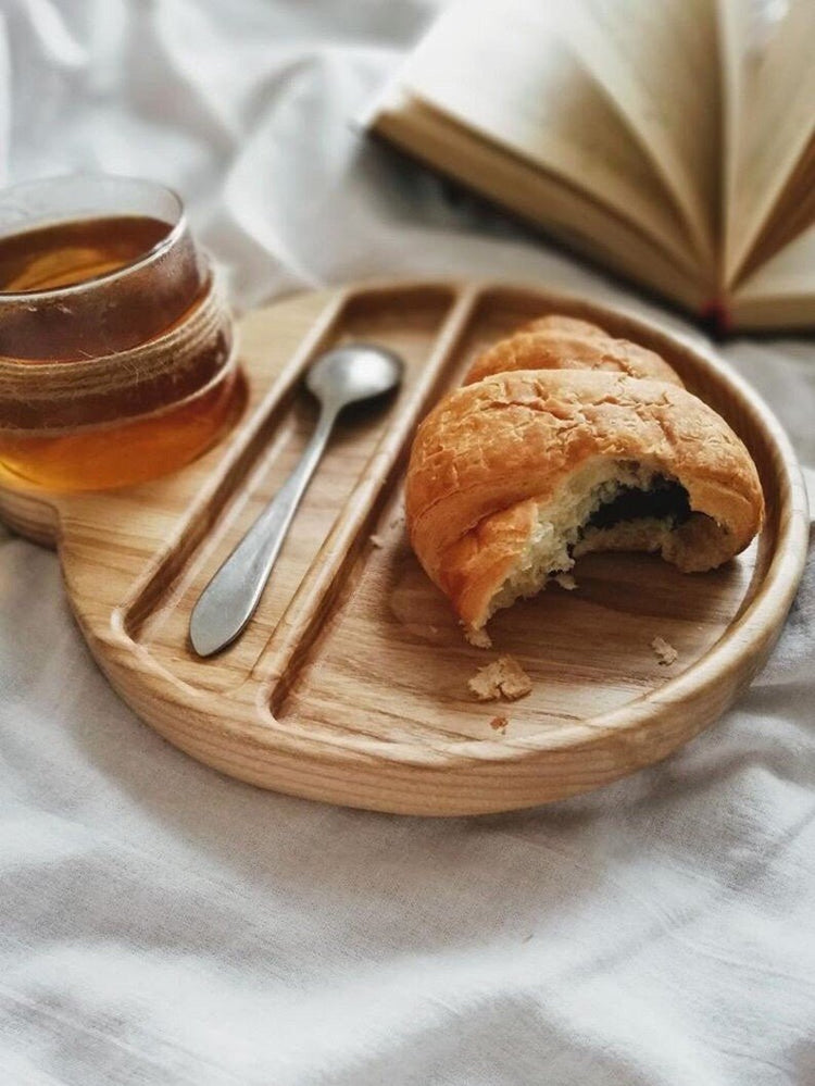 Wooden breakfast tray with bitten croissant, spoon and glass of tea