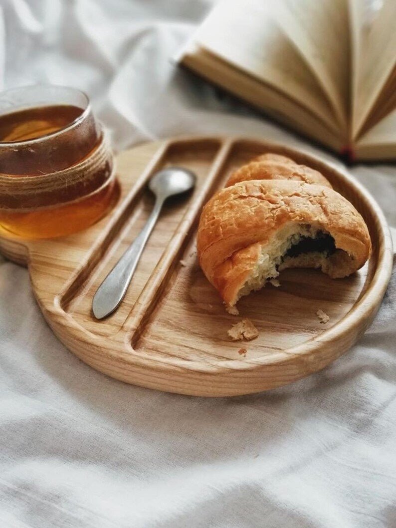 Wooden breakfast tray with bitten croissant, spoon and glass of tea