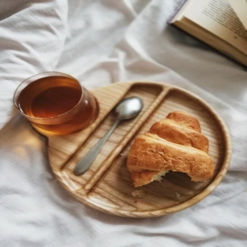 Close-up of wooden food tray with croissant and tea on white bedsheet