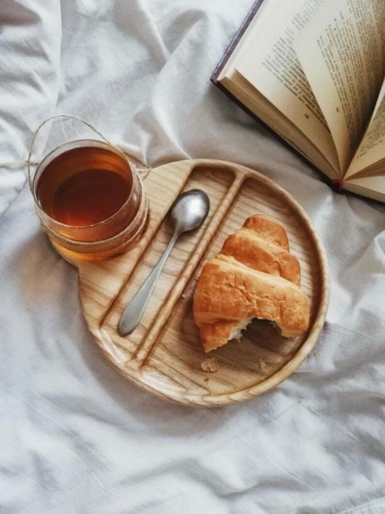 Cup and spoon wooden serving tray with pastry beside open book