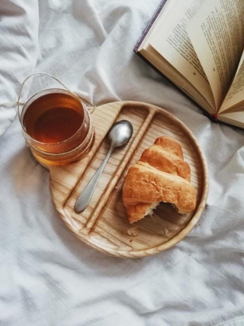 Cup and spoon wooden serving tray with pastry beside open book