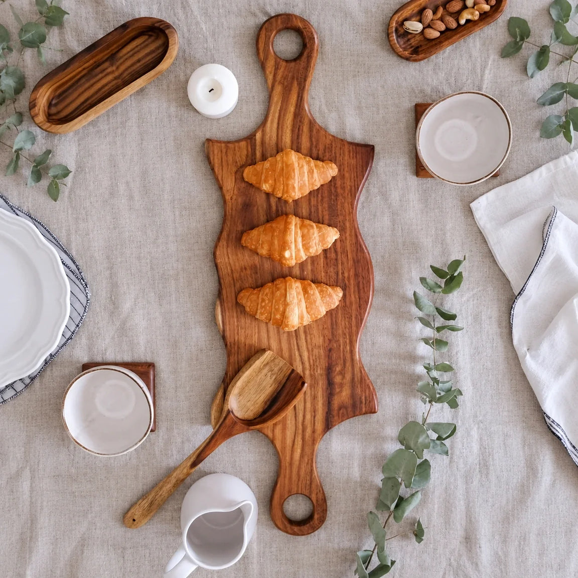 Double swirled wooden platter with handles on white table with herbs