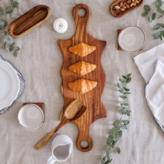 Double swirled wooden platter with handles on white table with herbs
