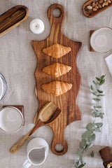Double swirled wooden platter with handles on white table with herbs