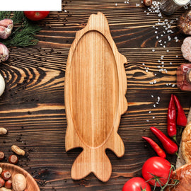 Fish shape wooden platter tray on dark table with chillies and tomatoes