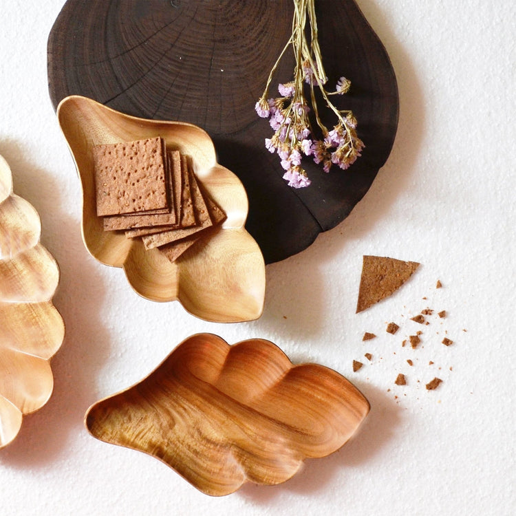 Two flake shaped wooden platters holding crackers beside dried flowers