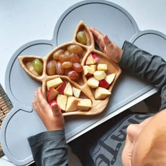 Child taking apple slices and snacks from fox shape wooden platter