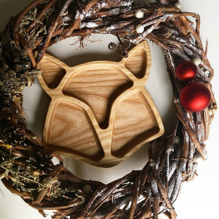 Empty fox shaped wooden serving platter inside twig wreath with red ornaments