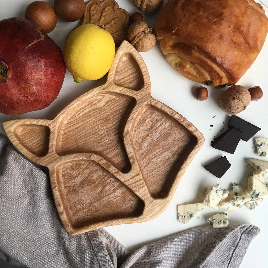 Dark finish fox shape wooden tray with apples, lemon and chocolate around it