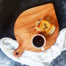 Leaf shaped wooden cheese platter with pastry and coffee on dark background