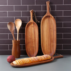 Two long wooden snack platters standing against grey tile wall with utensils
