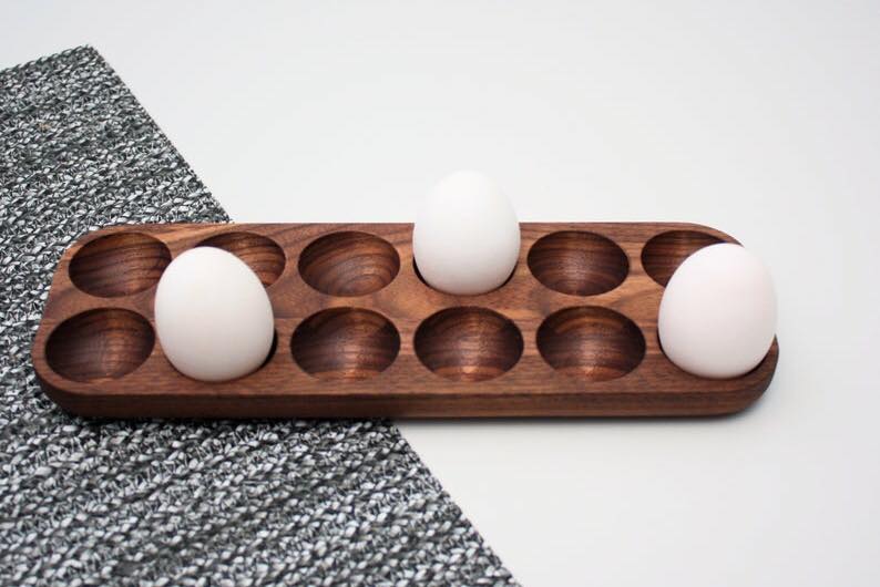 Side view of wooden egg holder tray with three white eggs on table