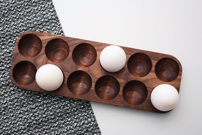 Wooden kitchen egg holder tray holding three white eggs beside grey cloth