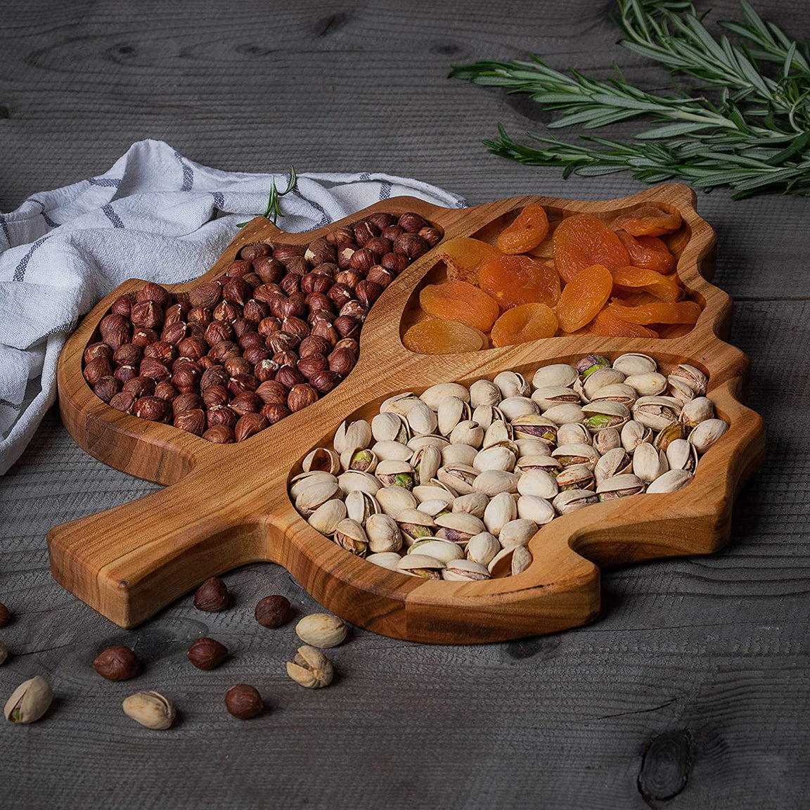 Leaf shaped wood dry fruit tray with nuts on dark wooden table, angled view