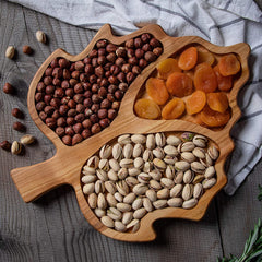 Maple leaf shaped wooden serving tray filled with hazelnuts, dried apricots and pistachios