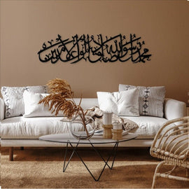 Black Muhammad Sadiq-ul-Amin calligraphy on brown wall above white sofa