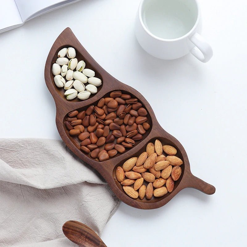 Leaf shaped wooden dry fruit snack tray with three sections of nuts beside cup