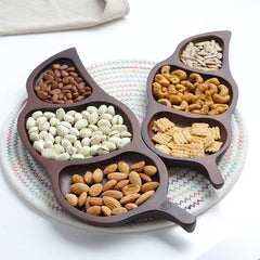Four leaf shaped wooden dry fruit trays arranged together on woven mat