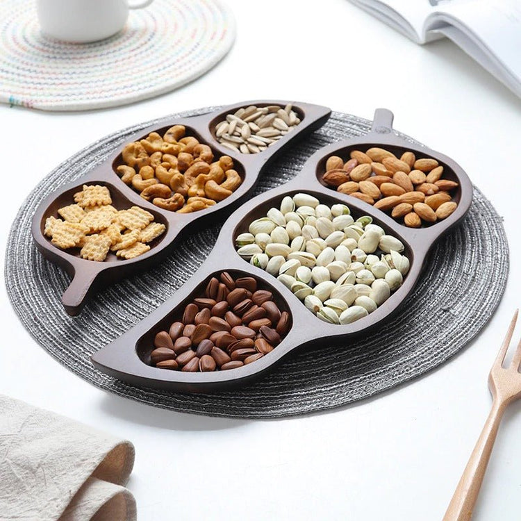 Wooden leaf snack trays filled with dry fruits arranged in circle on grey placemat