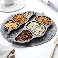 Wooden leaf snack trays filled with dry fruits arranged in circle on grey placemat