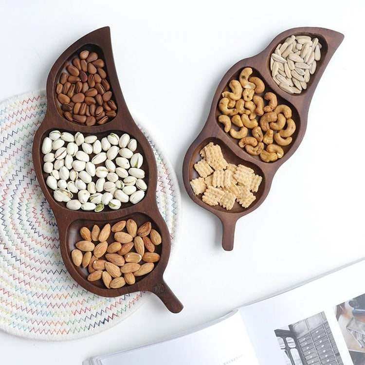Two dark wood leaf shaped snack trays filled with nuts and beans, top view