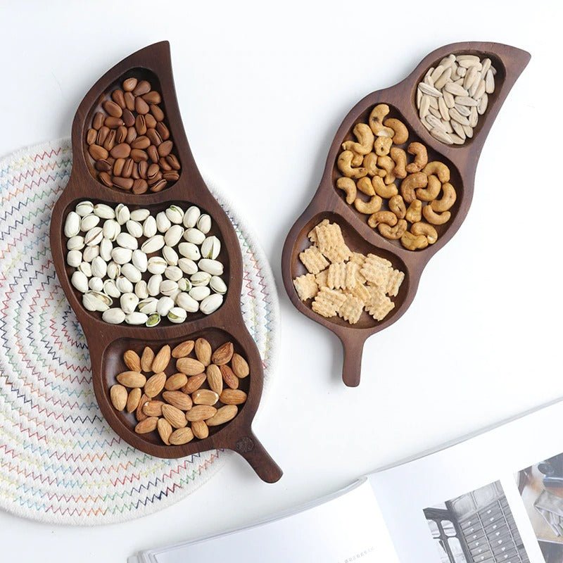 Two dark wood leaf shaped snack trays filled with nuts and beans, top view