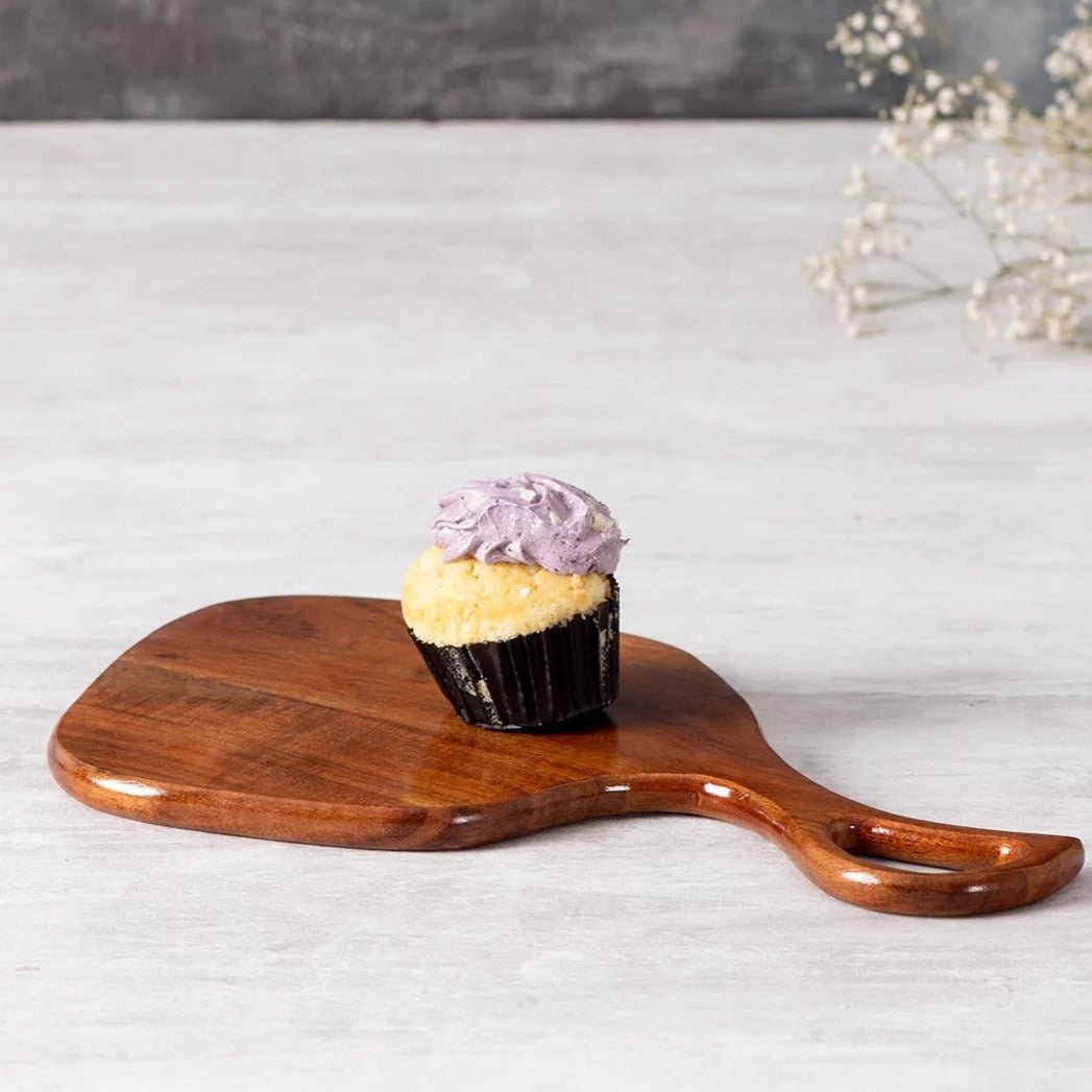 Solid wood serving tray with open handle holding a cupcake on marble surface