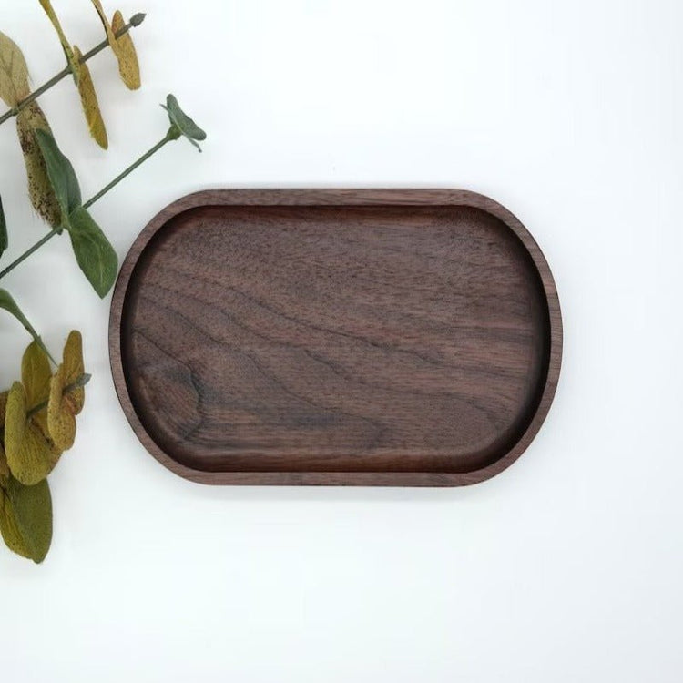 Oval dark wooden tray next to eucalyptus sprig on pale background