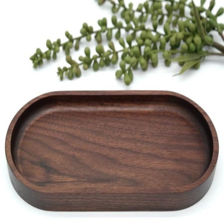 Close front view of deep oval walnut wood tray with greenery