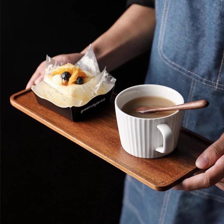 Person carrying rectangular wooden tea tray with coffee mug and pastry