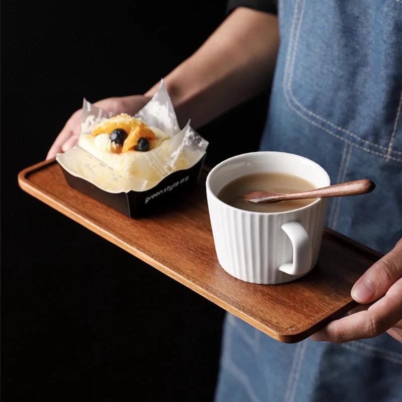 Person carrying rectangular wooden tea tray with coffee mug and pastry